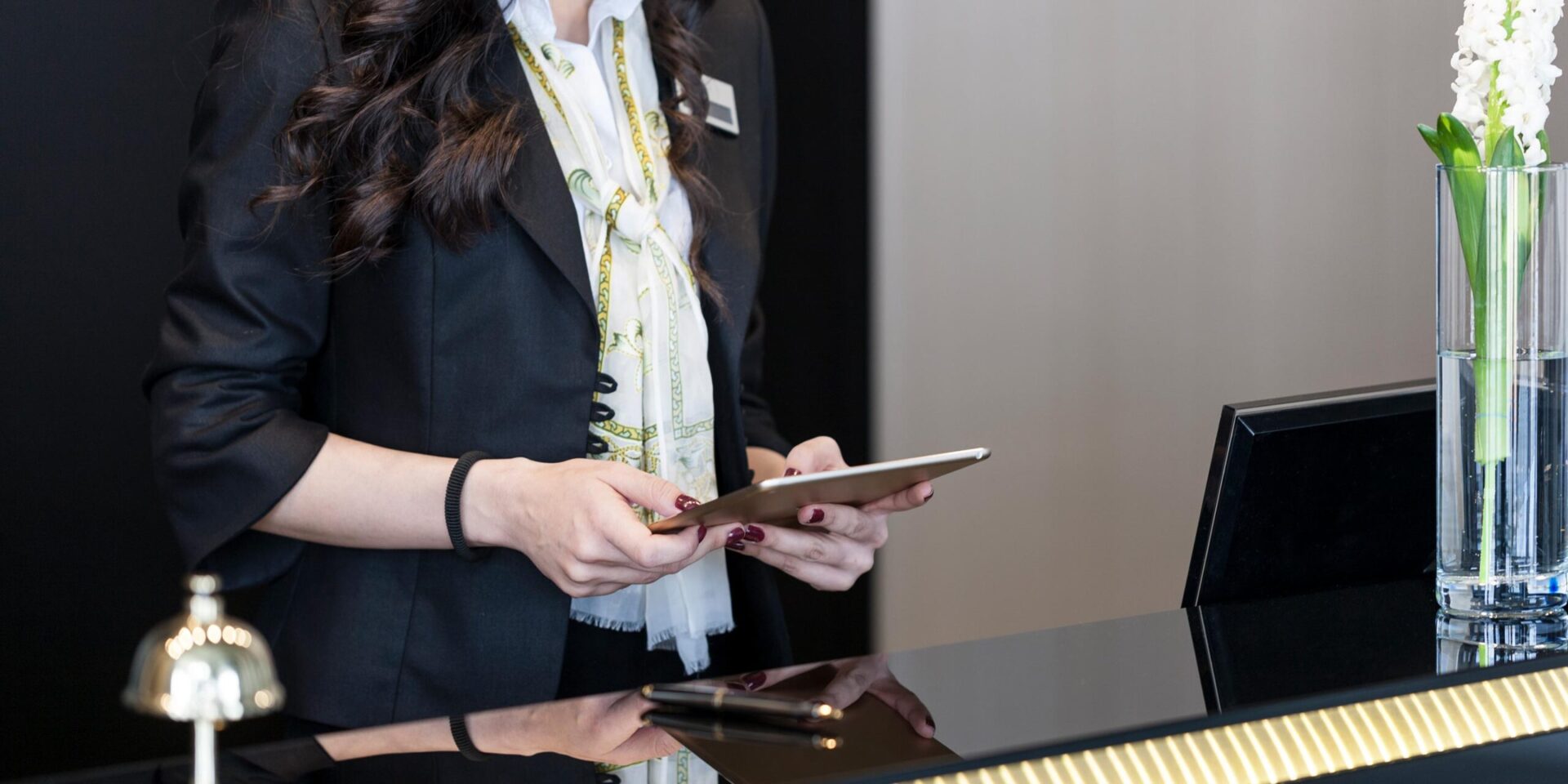 Close up image of hotel worker working on a tablet at the hotel front desk.