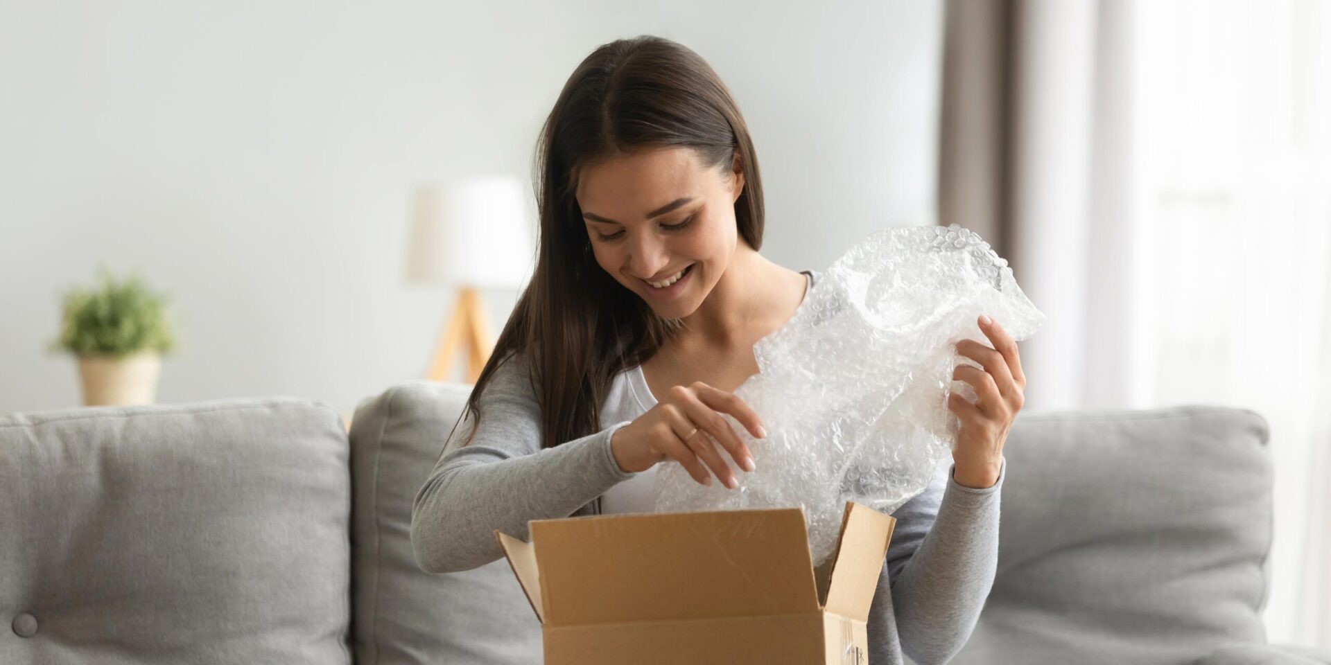 Image of woman sitting on couch unpacking a box.