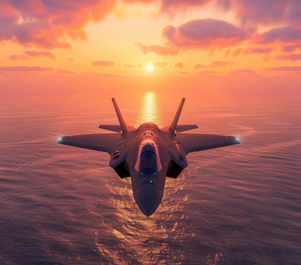 Image of a single-engine fighter jet flying over the ocean at sunset.