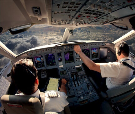 Photo taken from the back of an airplane cockpit showing two pilots flying a commercial airplane through the clouds.