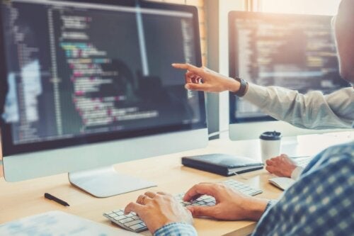 Two coders working on static analysis source code. Image showing two coders looking at monitor with code on the screen. One of the coders is pointing at the monitor, the other has hands on keyboard.